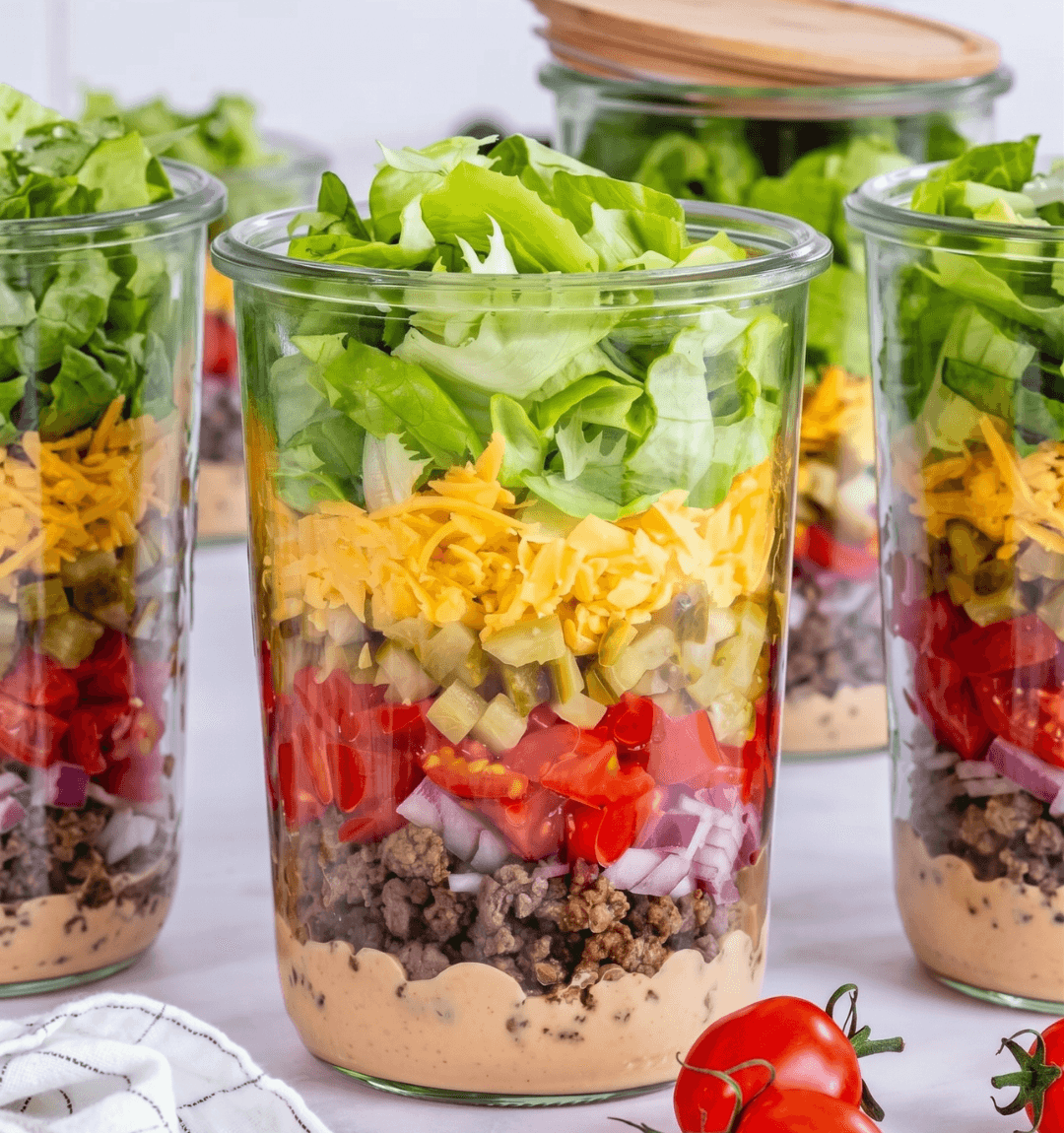 Três potes de salada em camadas com carne, queijo, tomate e alface